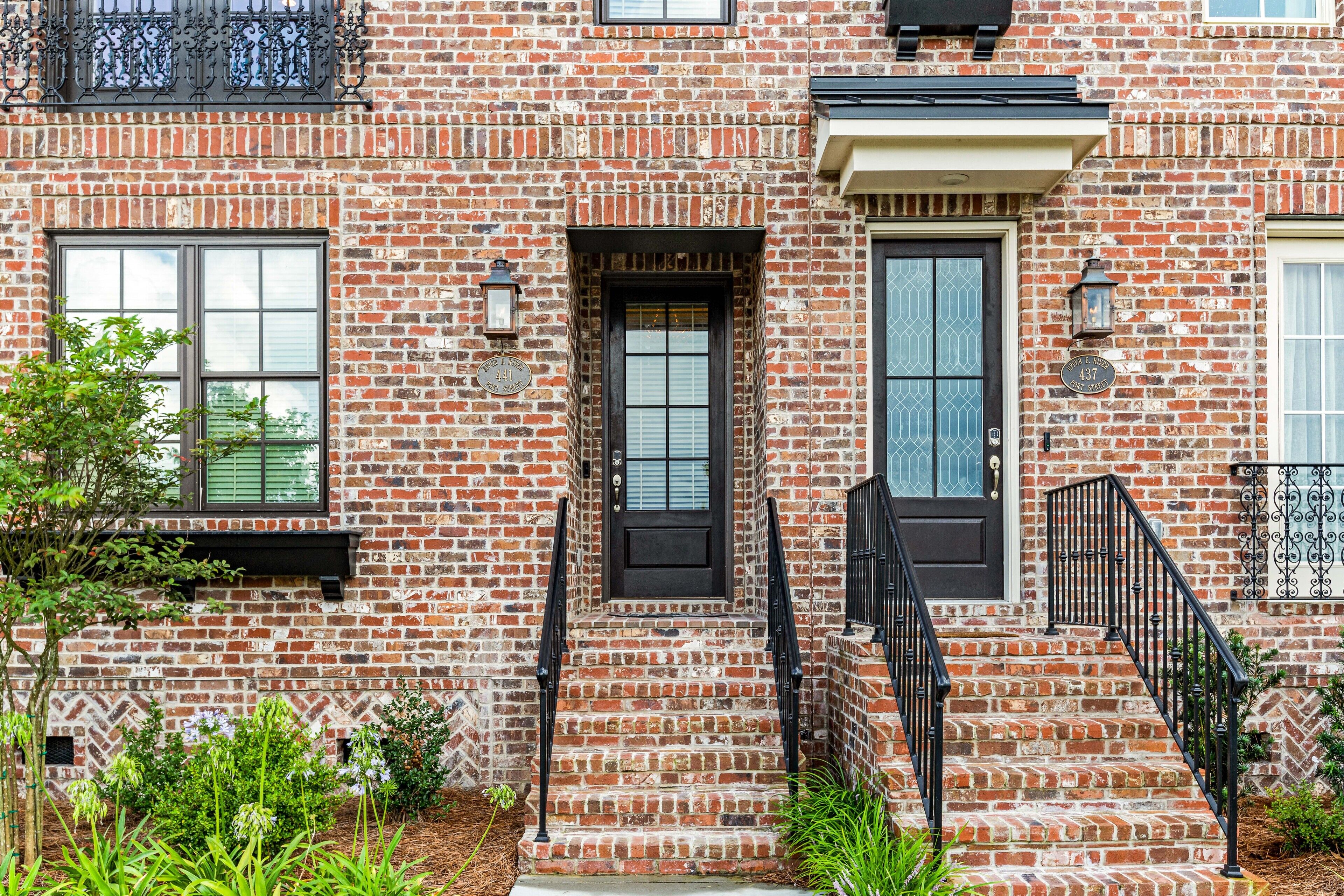 Un bâtiment en briques avec une porte d’entrée noire, un petit porche et une fenêtre ornée d’une grille décorative.