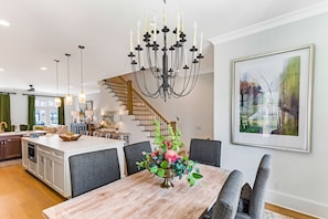 Una cocina amplia con una isla central, un comedor con candelabro y una escalera que conduce a un nivel superior.