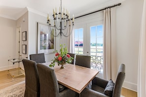 Un comedor con mesa de madera, sillas tapizadas en gris, una araña y vistas al exterior a través de amplios ventanales.