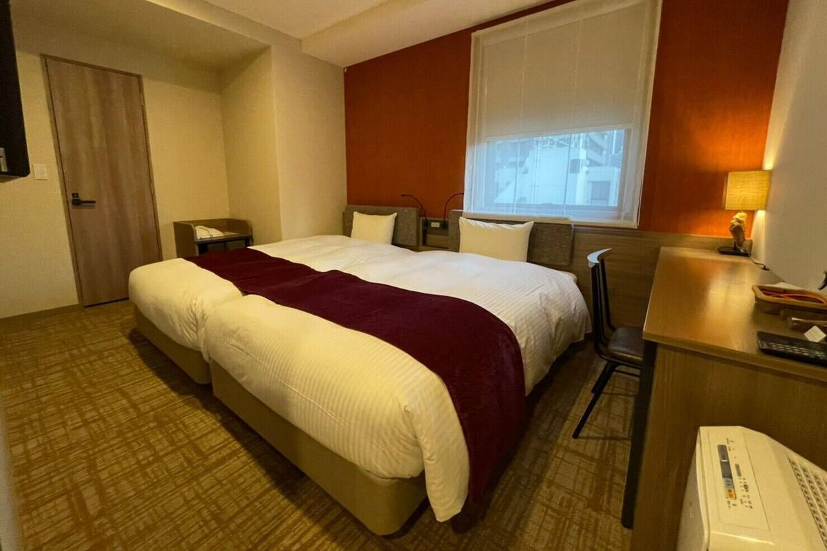 A hotel room with a large bed, a desk, a chair, a window, and a door.