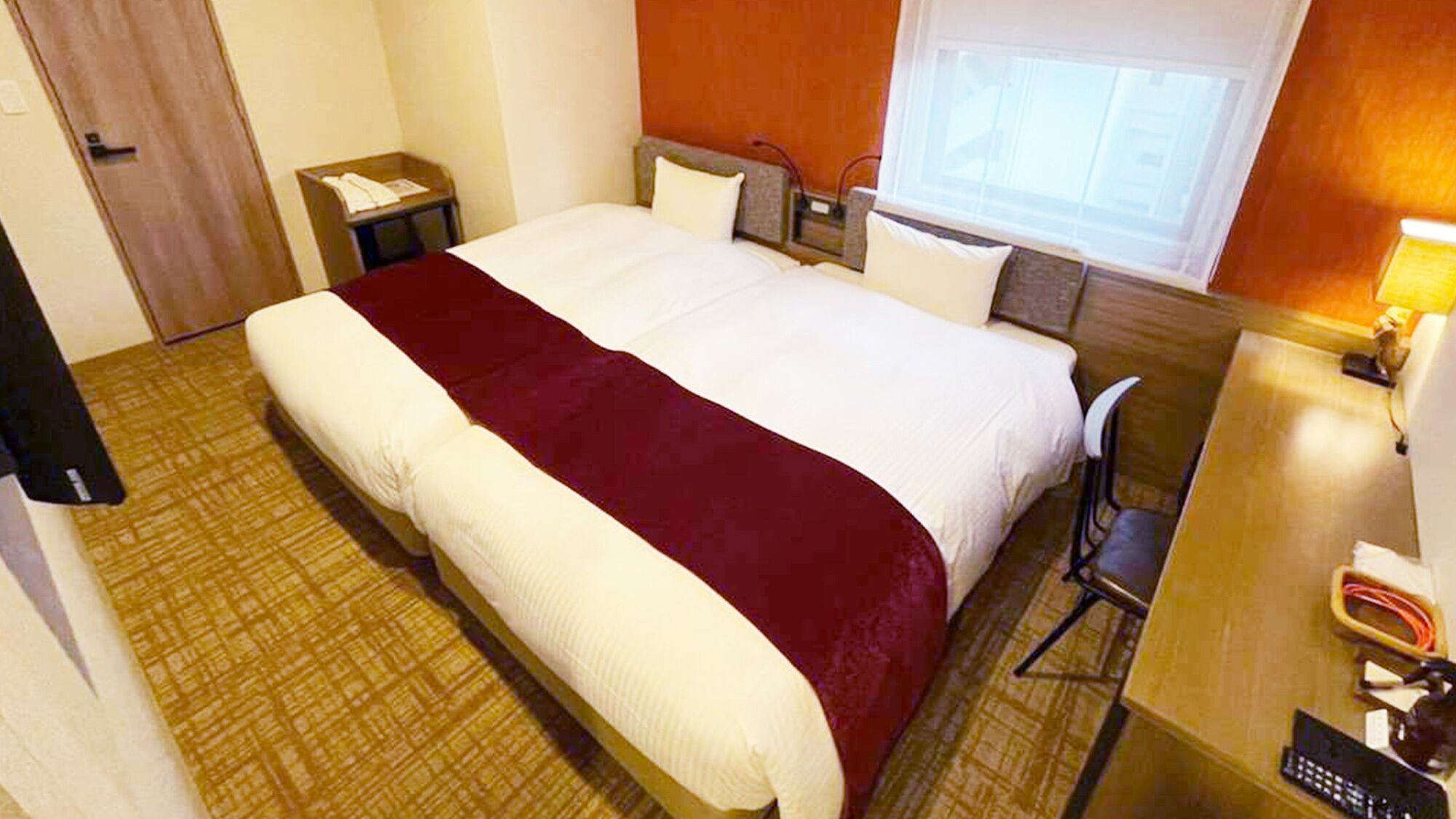 A hotel room with a bed, a desk, a chair, a nightstand, and a window.