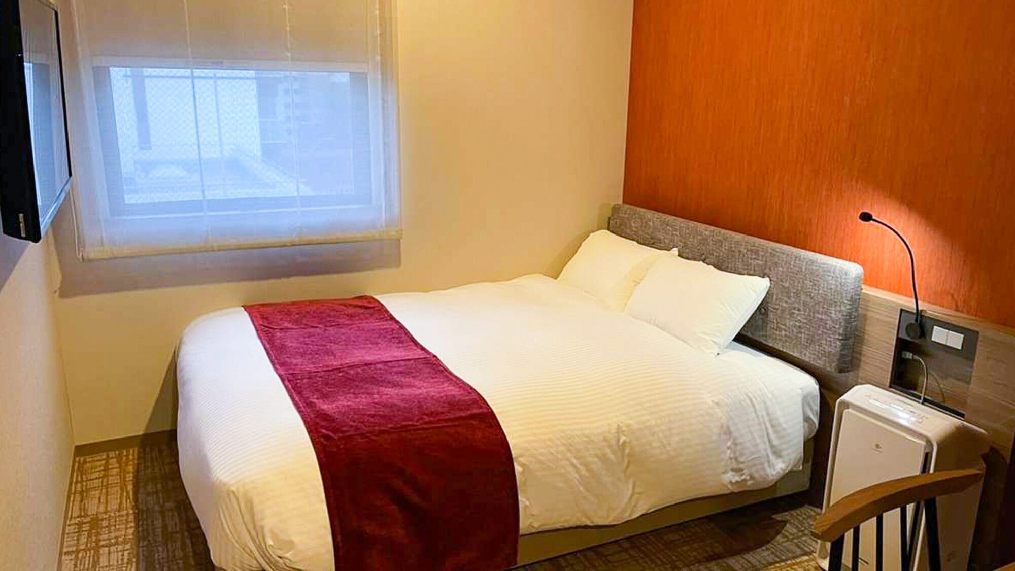 A hotel room with a bed, a TV, a bedside table, and a window.