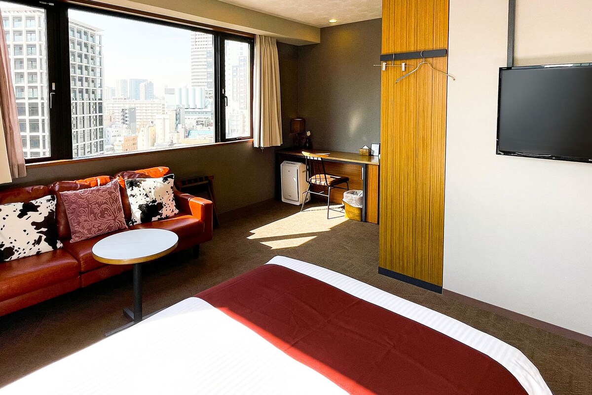 Une chambre d’hôtel avec un lit, un canapé, une petite table, une télévision et une vue sur la ville.