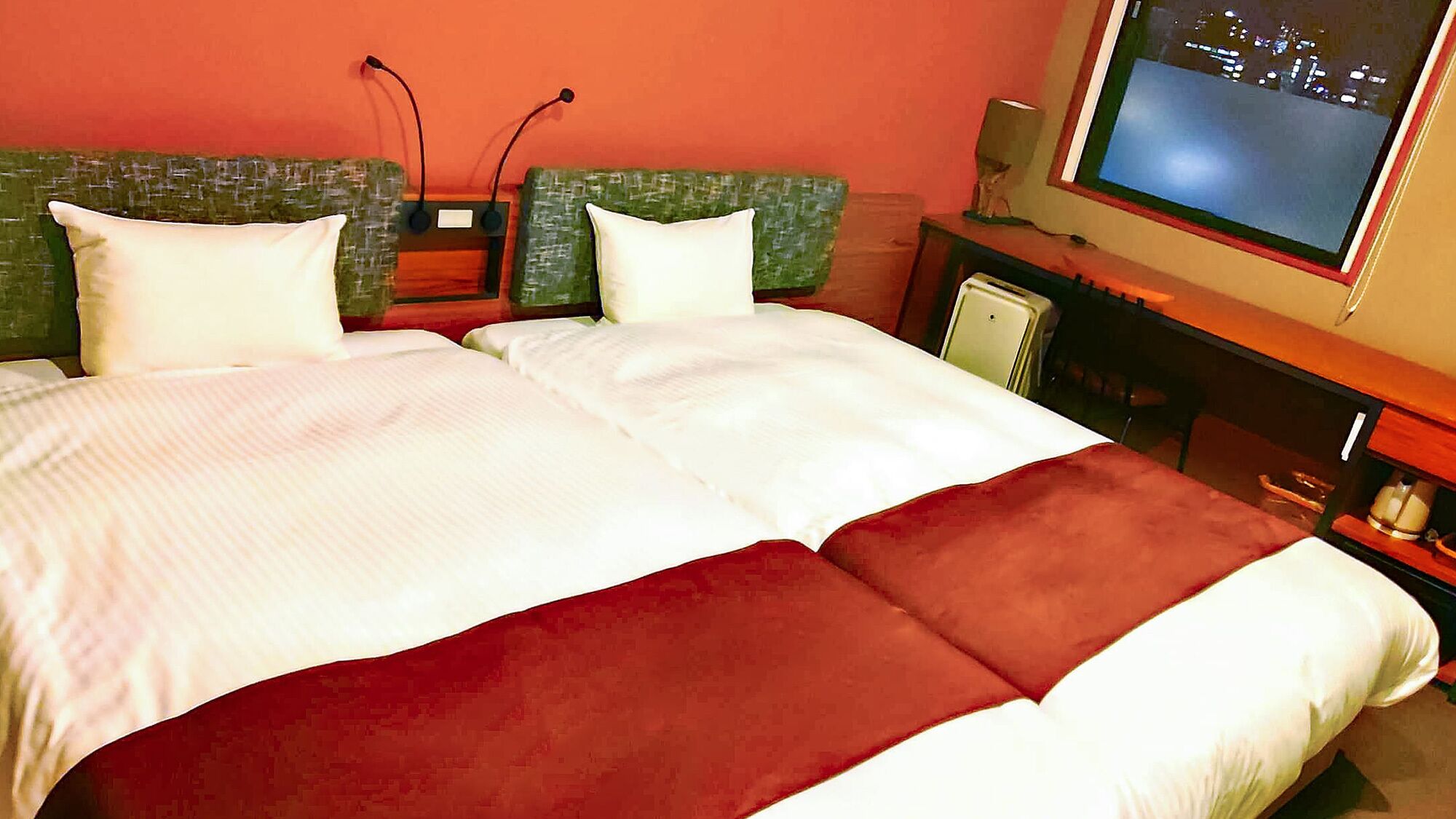 A hotel room with a bed, two pillows, a television, and a small table.