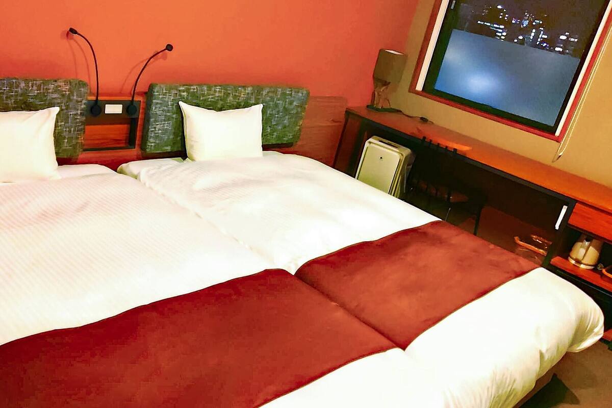 A hotel room with a bed, two pillows, a television, and a small table.
