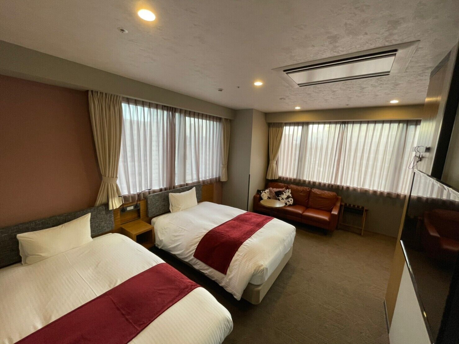 Quarto de hotel com duas camas, um sofá, uma mesa pequena e um espelho.
