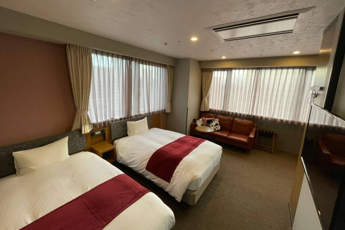 A hotel room with two beds, a sofa, a small table, and a mirror.