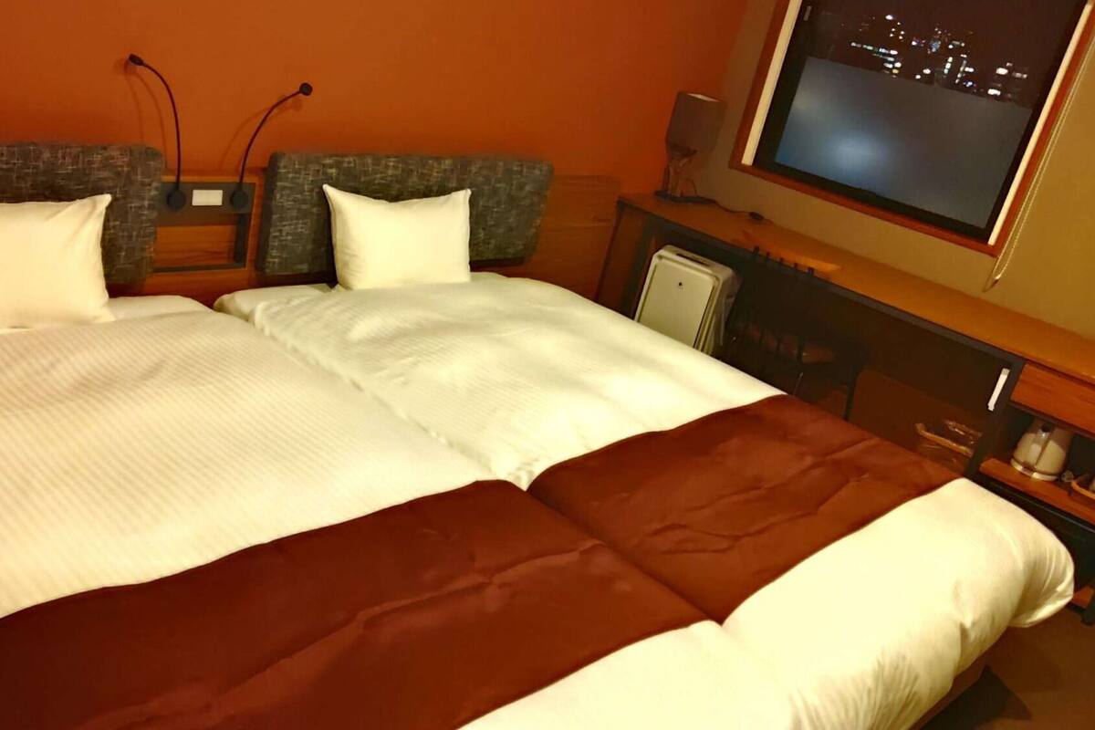 A double bed with white and brown bedding, a television on the wall, and a cityscape view.