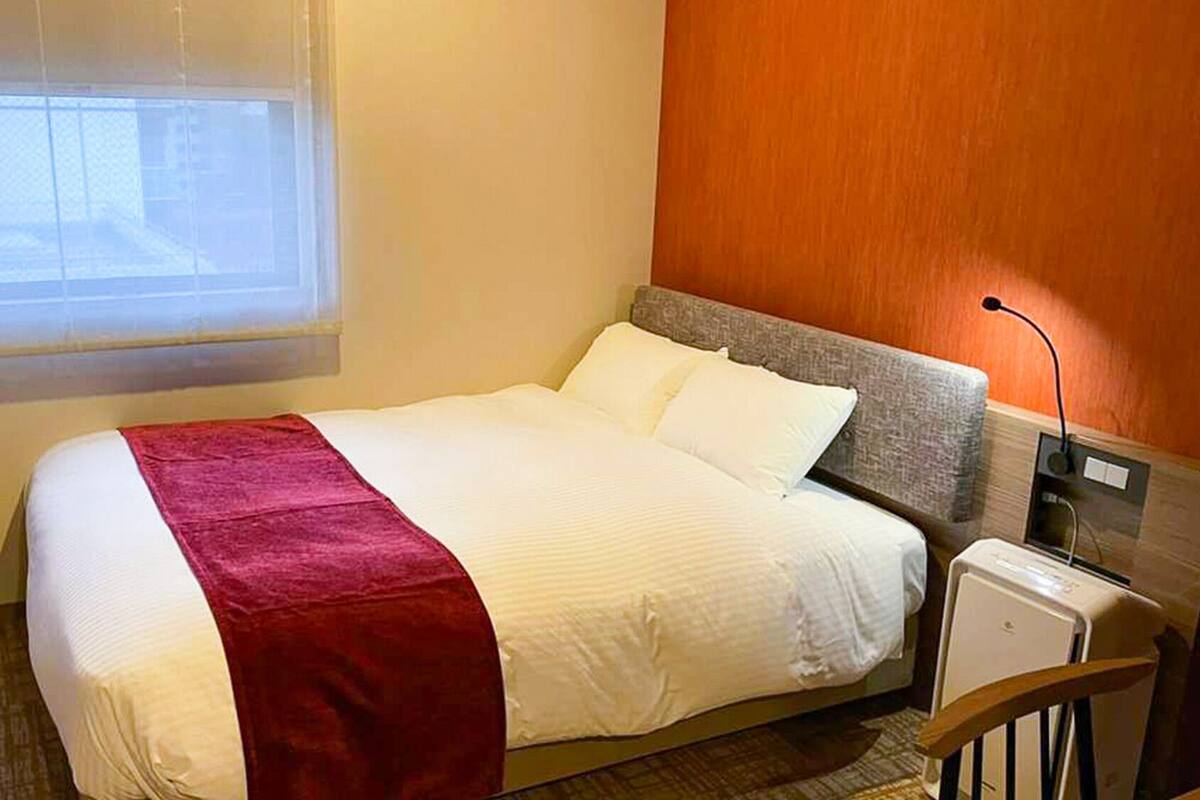 A hotel room with a bed, a TV, a bedside table, and a window.