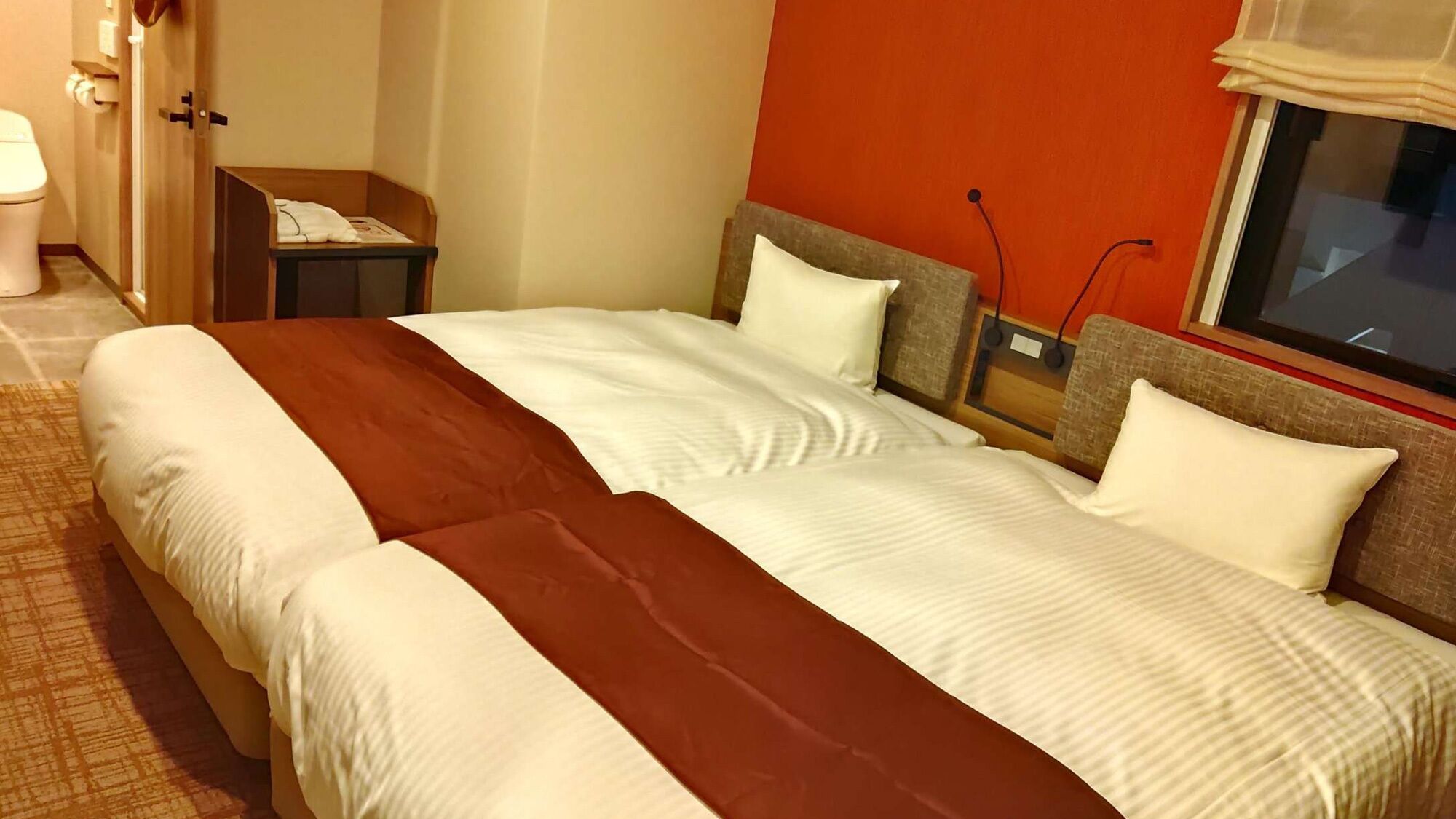 Quarto de hotel com cama de casal, mesa de cabeceira, janela com vista e banheiro com vaso sanitário e pia.