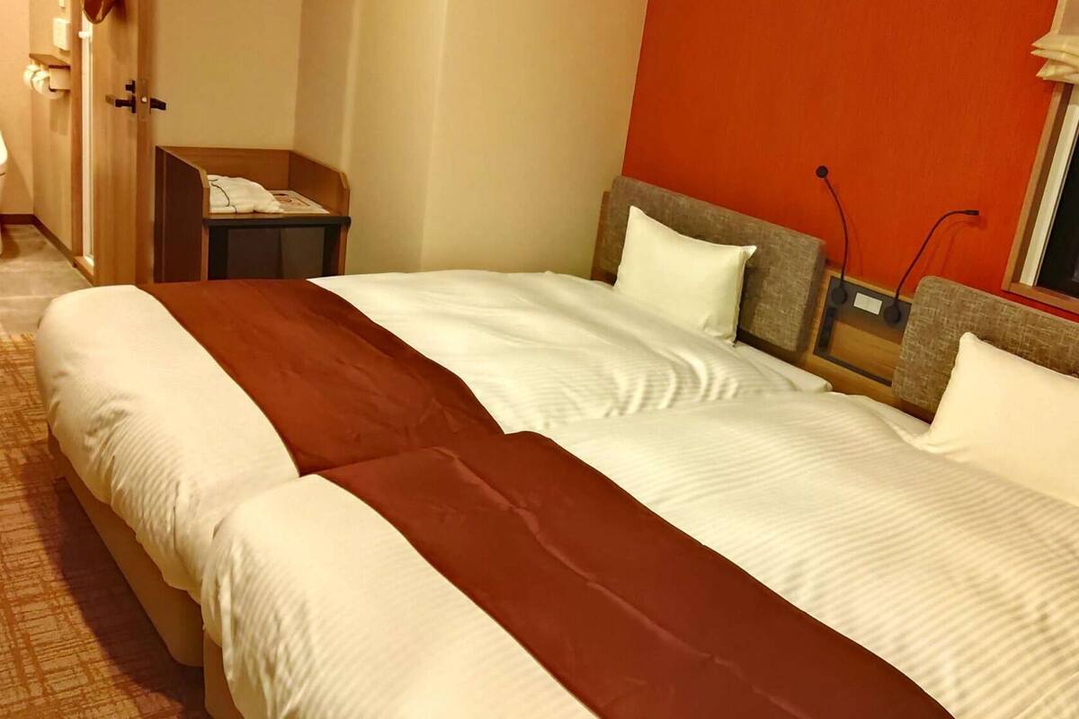 A hotel room with a double bed, a bedside table, a nightstand, a window with a view, and a bathroom with a toilet and sink.
