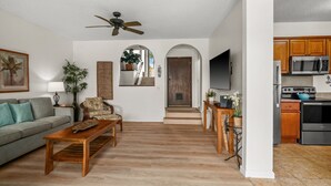 A spacious living room with a wooden coffee table, a grey sofa, and a ceiling fan. - 1Br 1Ba Kahala Tropical Dream, Pool, Garden View 513 (Koloa)