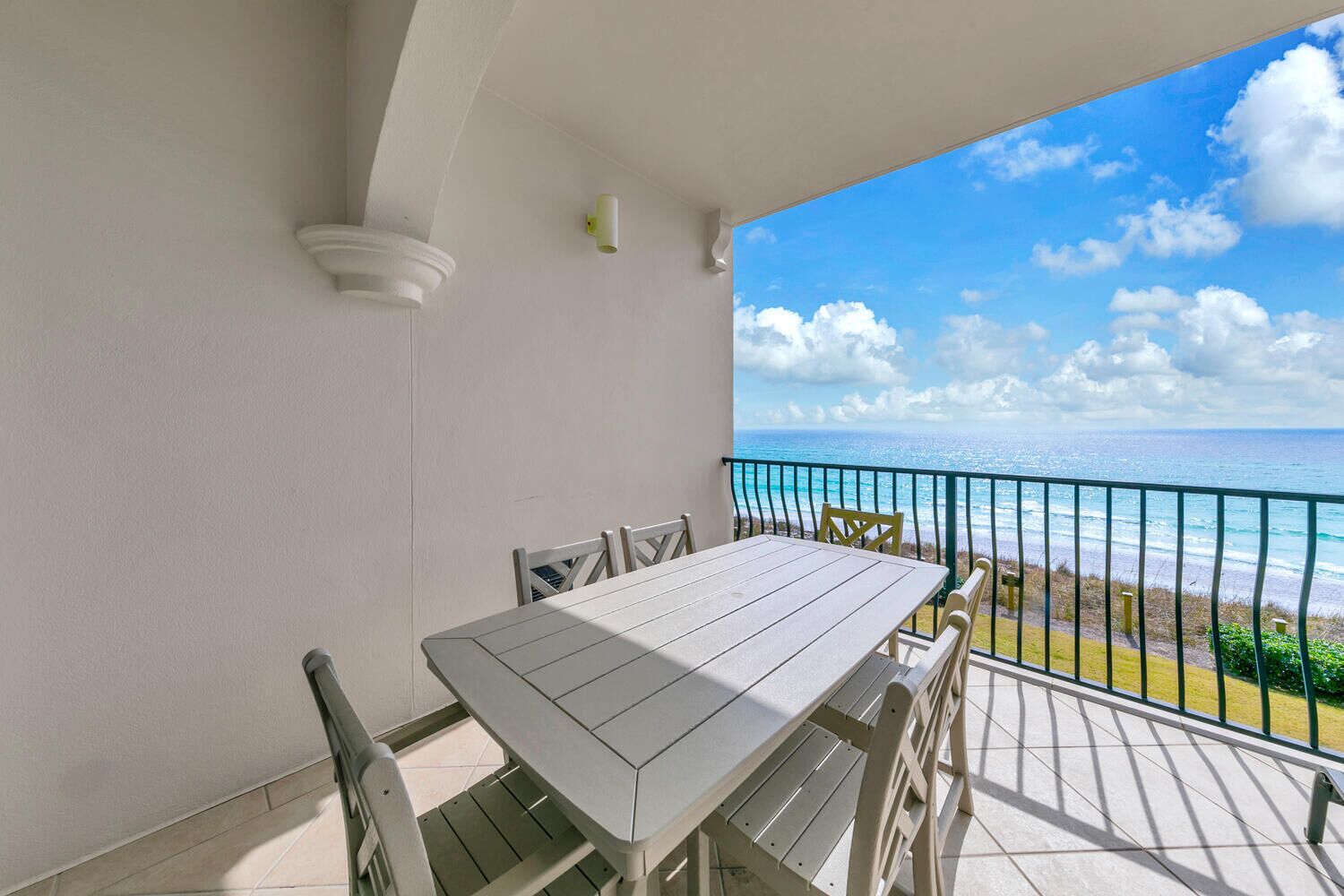 A balcony with a table and chairs, overlooking a beach with a clear sky and ocean.