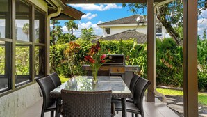 Eine Terrasse im Freien mit einem Tisch aus Glas, Korbstühlen und einem Grill.