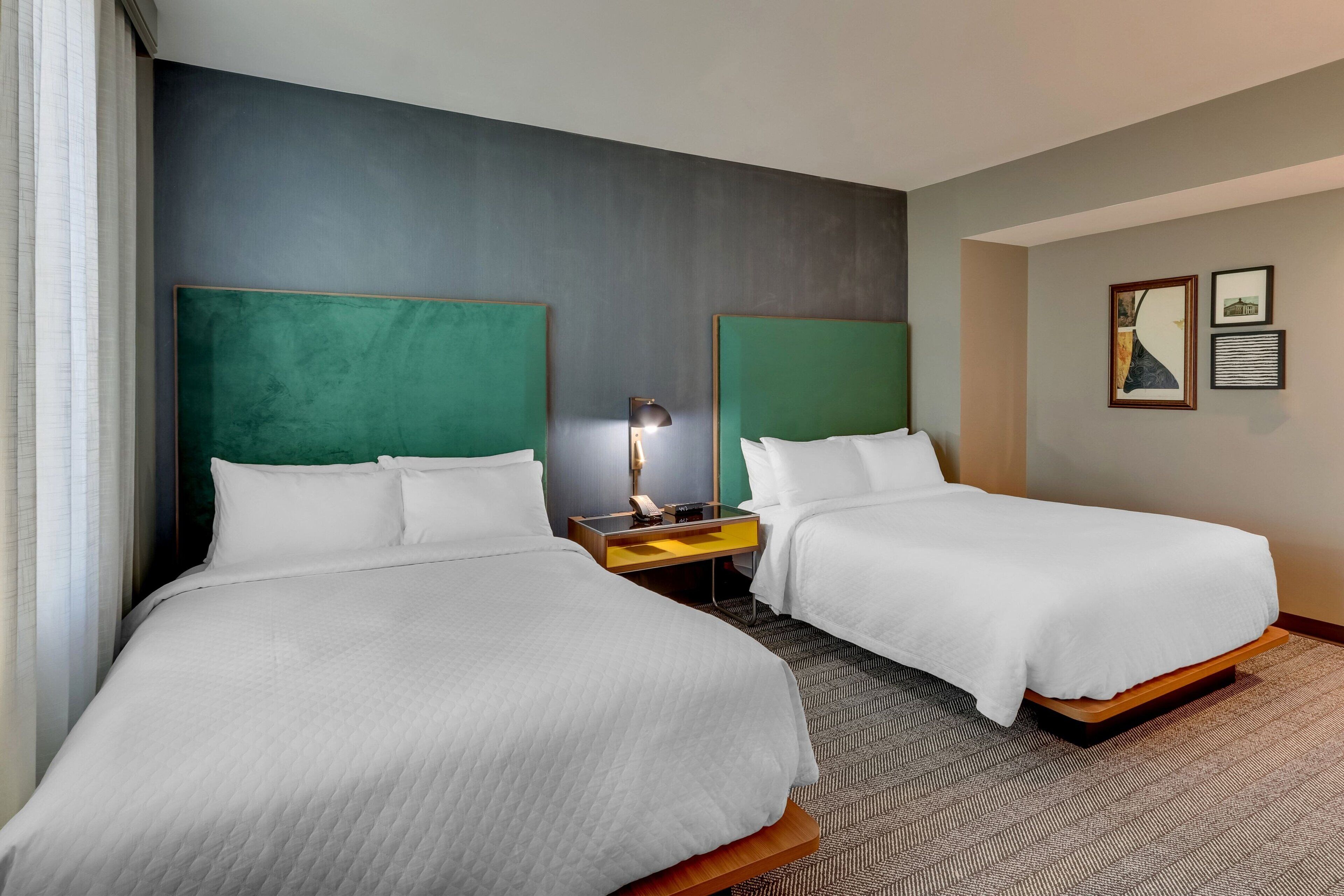 A hotel room with two beds, a nightstand with a lamp, and a wall with framed pictures.