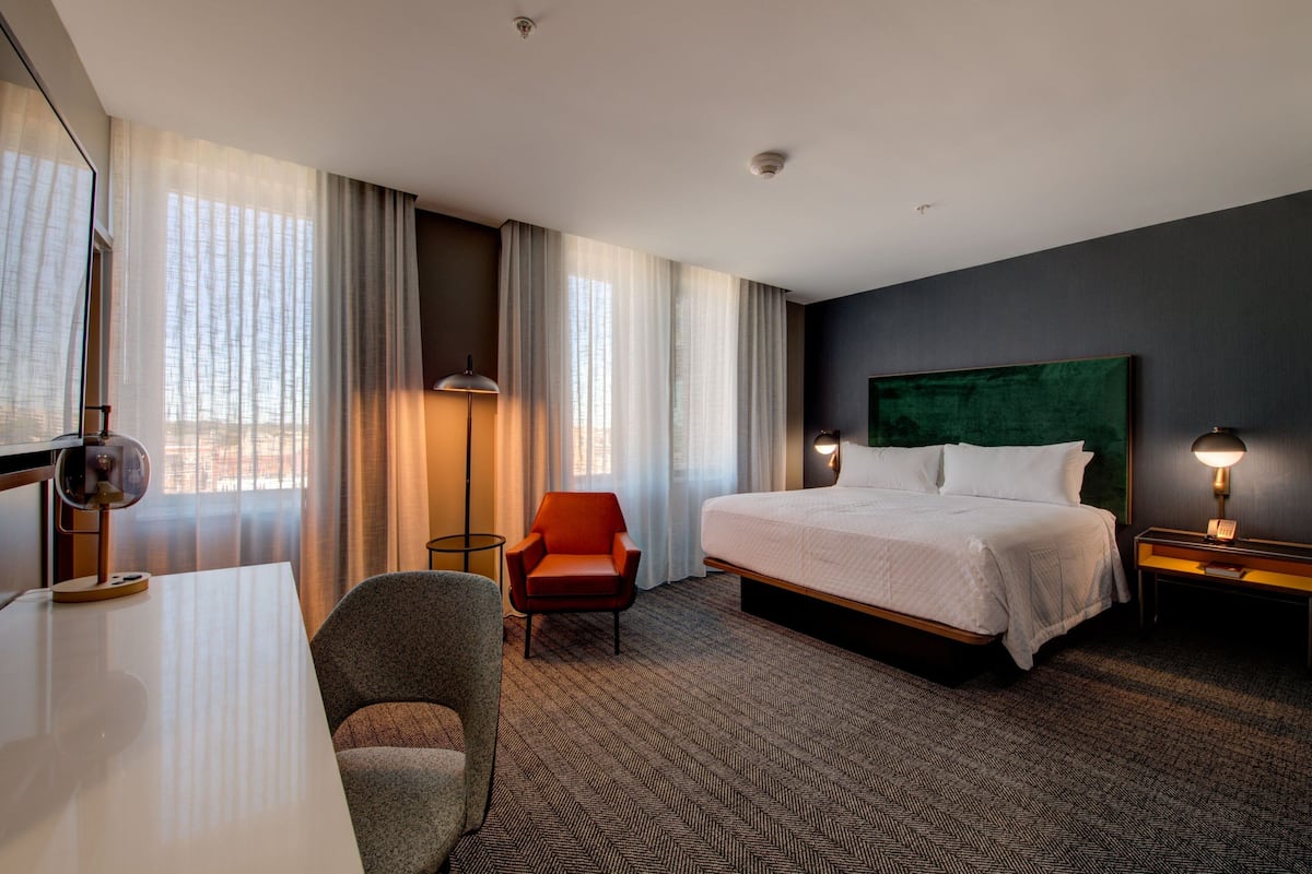 A hotel room with a large bed, a desk, a chair, and a lamp.