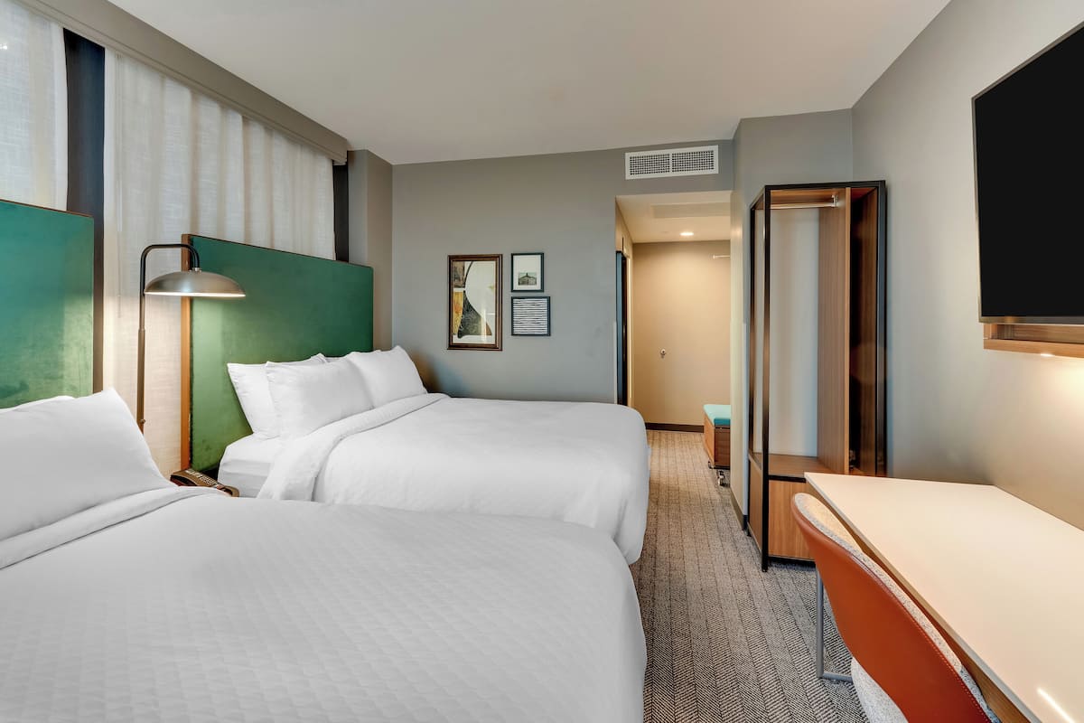 A hotel room with two beds, a desk, a chair, a TV, and a door leading to a bathroom.
