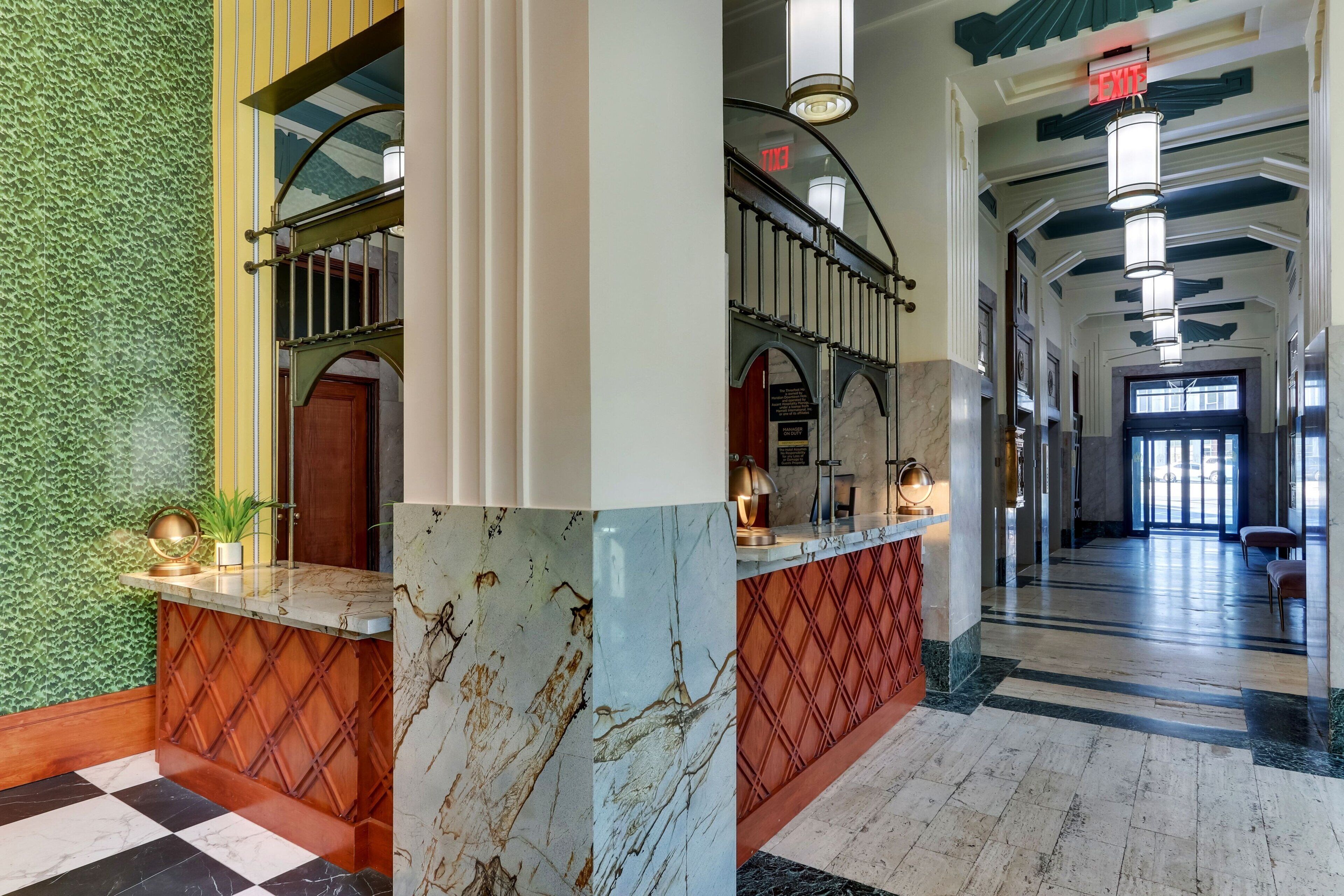 A lobby with a checkered floor, a reception desk, a staircase, and a green textured wall.
