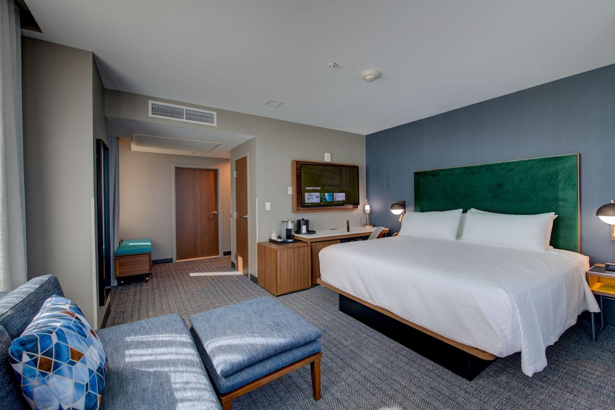 A hotel room with a large bed, a desk, a chair, and a small table.