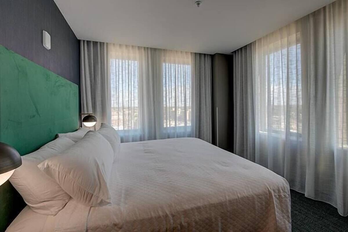 A hotel room with a large bed, a headboard, a bedside lamp, and sheer curtains.