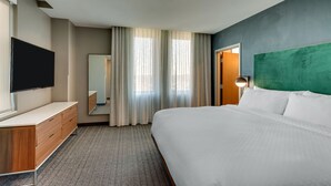 Quarto de hotel com cama, televisão, penteadeira, espelho e uma parede verde decorativa.