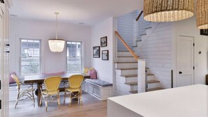 A modern kitchen with a dining area, featuring a staircase and wicker pendant lights. - Mid island oasis! 3-bedroom, 4 bath in the middle of “second downtown” (Nantucket)
