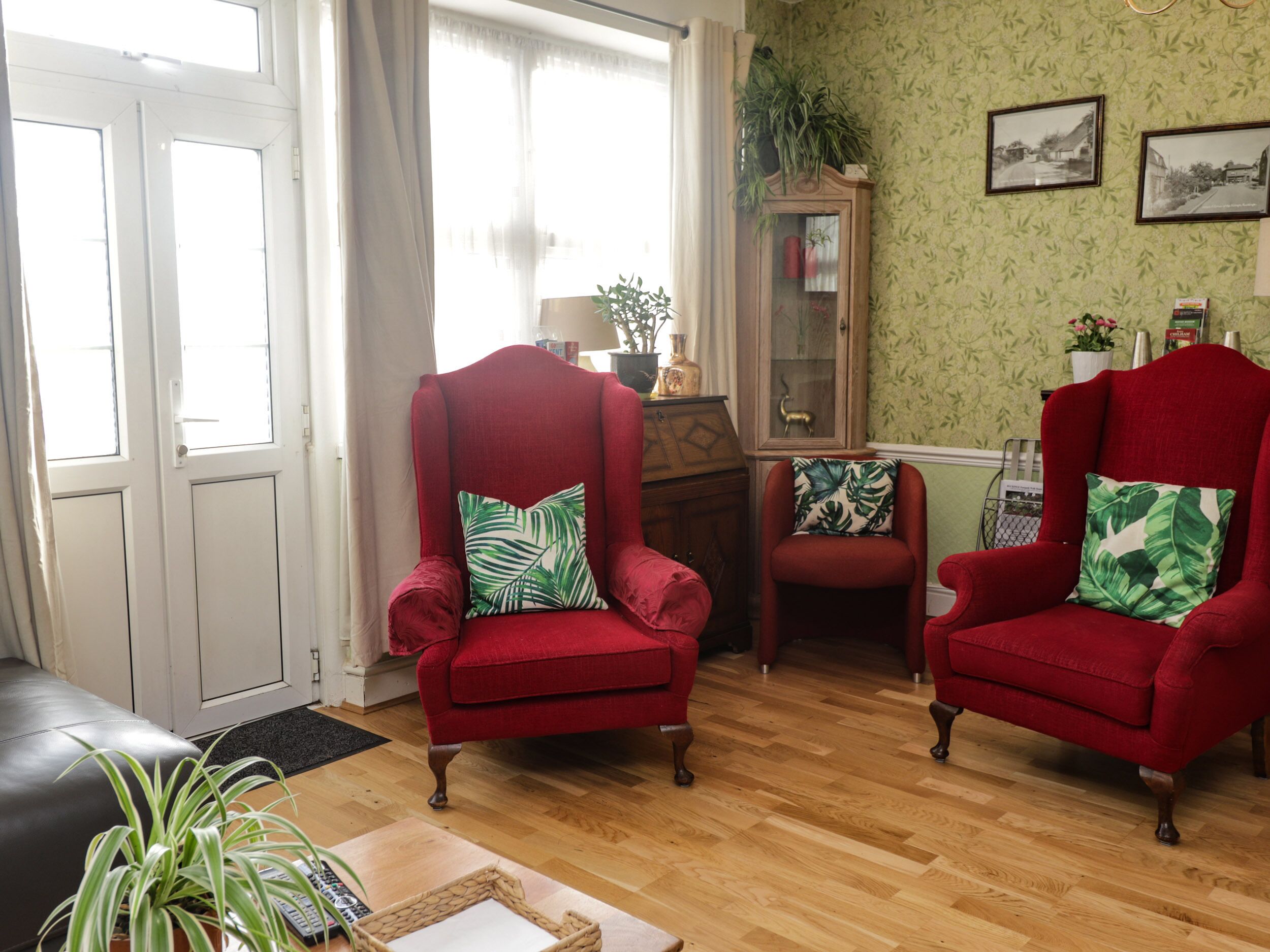 Una sala con dos sillones rojos, un aparador de madera y una pared estampada en verde.