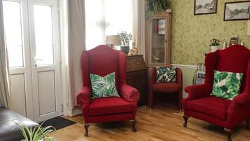 Una sala con dos sillones rojos, un aparador de madera y una pared estampada en verde.