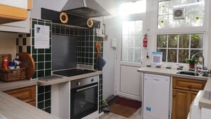 A compact kitchen with a stove, oven, and dishwasher. There is a window with a view of trees and a fire extinguisher mounted on the wall. - Old Post Office (Ashford)