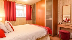 A bedroom with a bed, a wardrobe, a vanity with a mirror, and a red chair. - Old Post Office (Ashford)