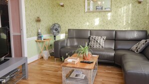 A living room with a leather sofa, a wooden coffee table, a TV stand, a fan, and a mirror on the wall. - Old Post Office (Ashford)
