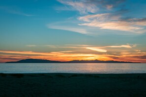 A beach with a sunset over the water and distant mountains. - 1551 Mandalay Beach Road (Oxnard)