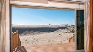 Varanda com vista para uma praia arenosa e céu claro.