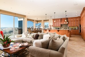 A spacious living area with a large sofa, a coffee table with decorative items, and a view of the ocean through large windows.