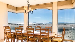 Uma sala de jantar com uma mesa grande e cadeiras, janelas amplas com vista para a praia.