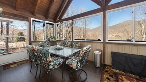 A dining area with a wooden ceiling, large windows, and a table with floral chairs. - Halfback Ridge -Hot Tub-Magnificent Views-Motorcycle & Pet-Friendly-Fenced Yard
 (Maggie Valley)