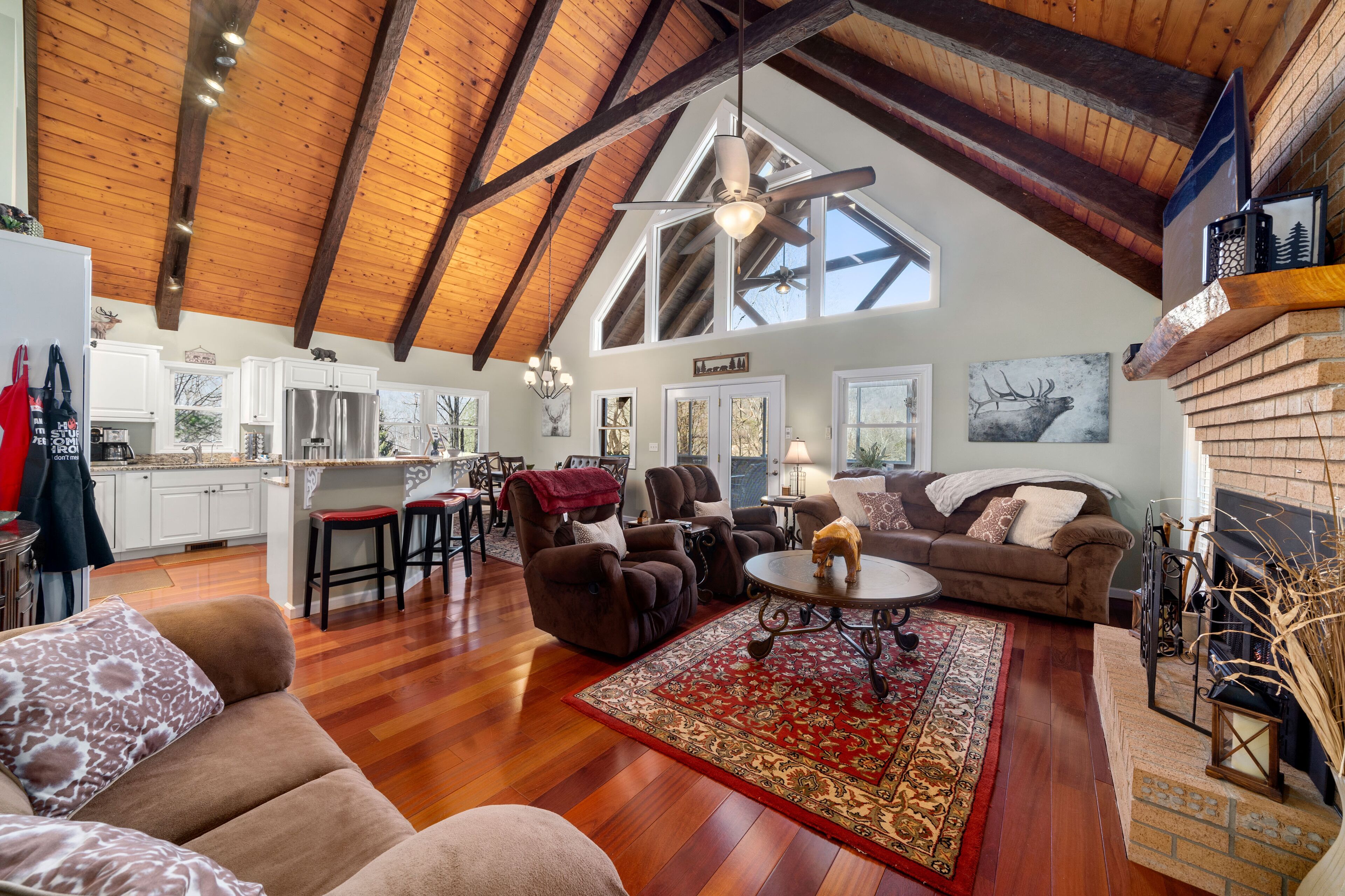 A spacious living area with a high ceiling, wooden beams, a fireplace, and a large window.
