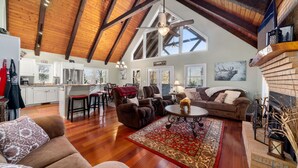 A spacious living area with a high ceiling, wooden beams, a fireplace, and a large window. - Halfback Ridge -Hot Tub-Magnificent Views-Motorcycle & Pet-Friendly-Fenced Yard
 (Maggie Valley)
