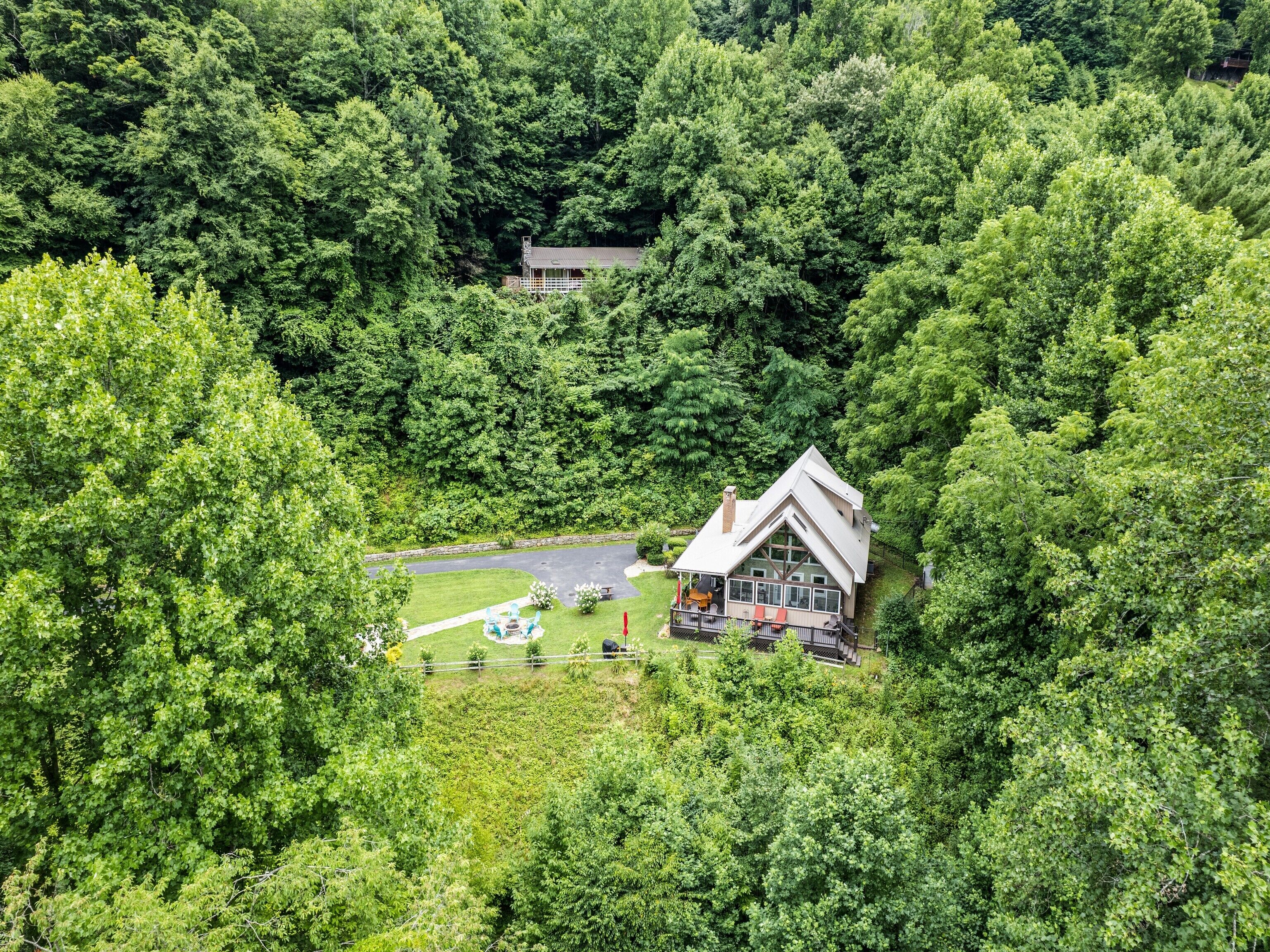 A lodge surrounded by dense forest, with a large deck and outdoor seating area.