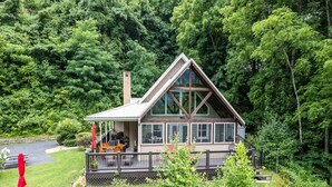 A cabin with a deck, surrounded by dense forest. - Halfback Ridge -Hot Tub-Magnificent Views-Motorcycle & Pet-Friendly-Fenced Yard
 (Maggie Valley)