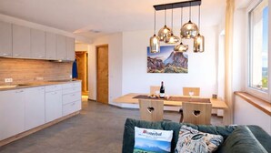 A modern kitchen with white cabinets, a dining area with a wooden table and chairs, and a green sofa with a pillow. - Binterhof vacation apartment GENZIANA (Trentino-Alto Adige)