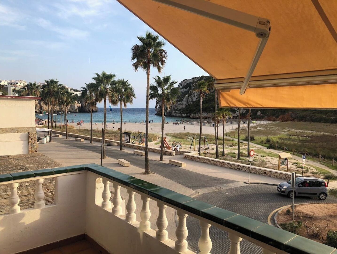 Een balkon met uitzicht op een strand, palmbomen en een rotsachtige klif.