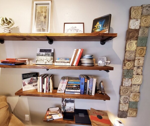 Three wooden shelves with books, a camera, and decorative items. - The Carriage House in SoMa (Little Rock)