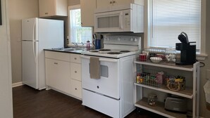 A kitchen with white cabinets, a white refrigerator, a stove, a microwave, and a window with blinds. - The Carriage House in SoMa (Little Rock)