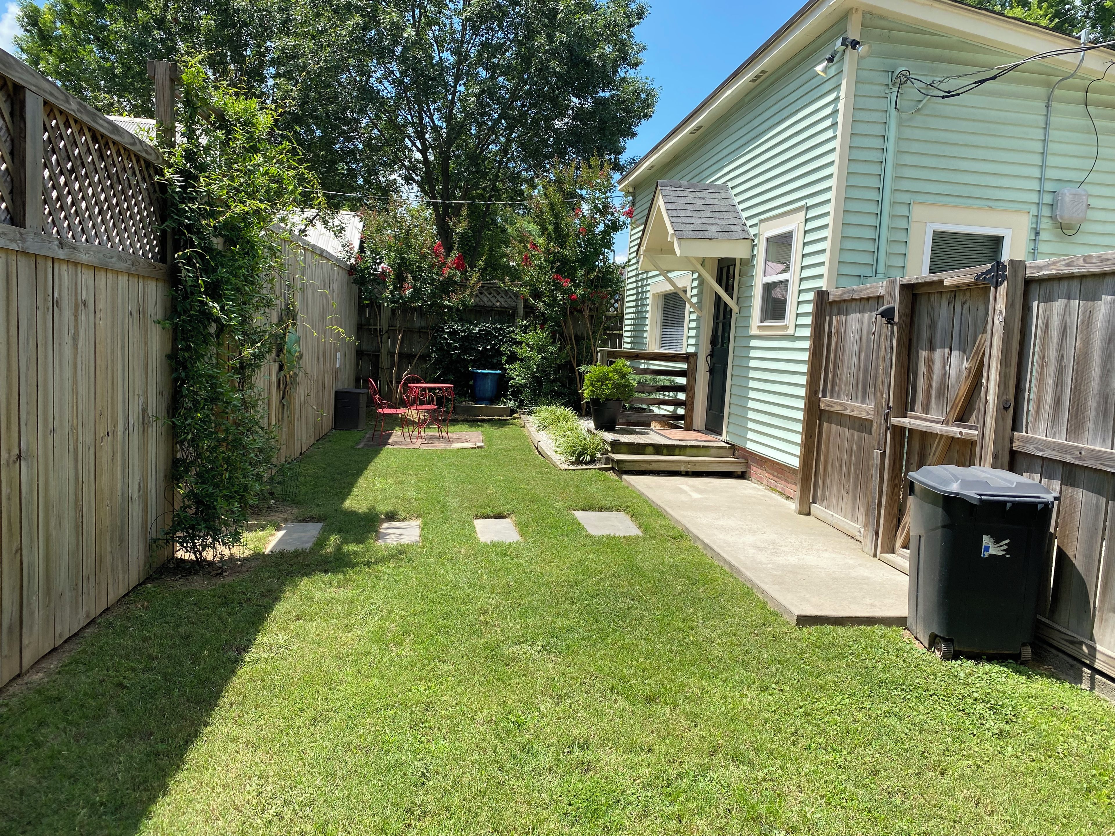 A backyard with a wooden fence, a small patio, and a house.