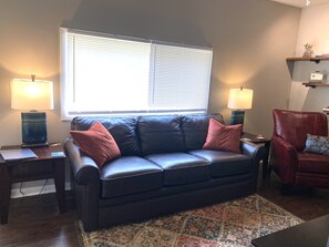 A dark leather sofa with two red cushions, a patterned rug, and two lamps on side tables. - The Carriage House in SoMa (Little Rock)