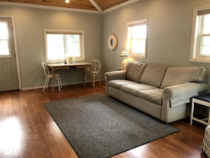 A living room with a wooden floor, a striped sofa, a dining table with chairs, and a rug.