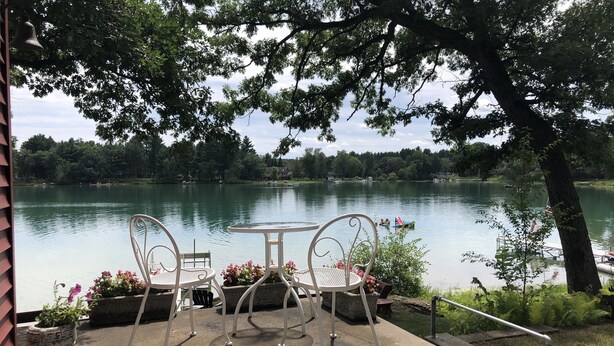Ein Sitzbereich im Freien mit Metallstühlen und einem Tisch, mit Blick auf einen See und Boote.