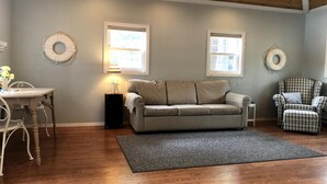 Ein geräumiges Wohnzimmer mit Holzboden, einem gestreiften Sofa, einem karierten Sessel und einem Essbereich mit Tisch und Stühlen.