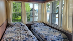 A room with two beds, wooden walls, large windows with curtains, and a view of a house and greenery outside. - "Uptacamp" feel, true Maine style Camp (Lincolnville)